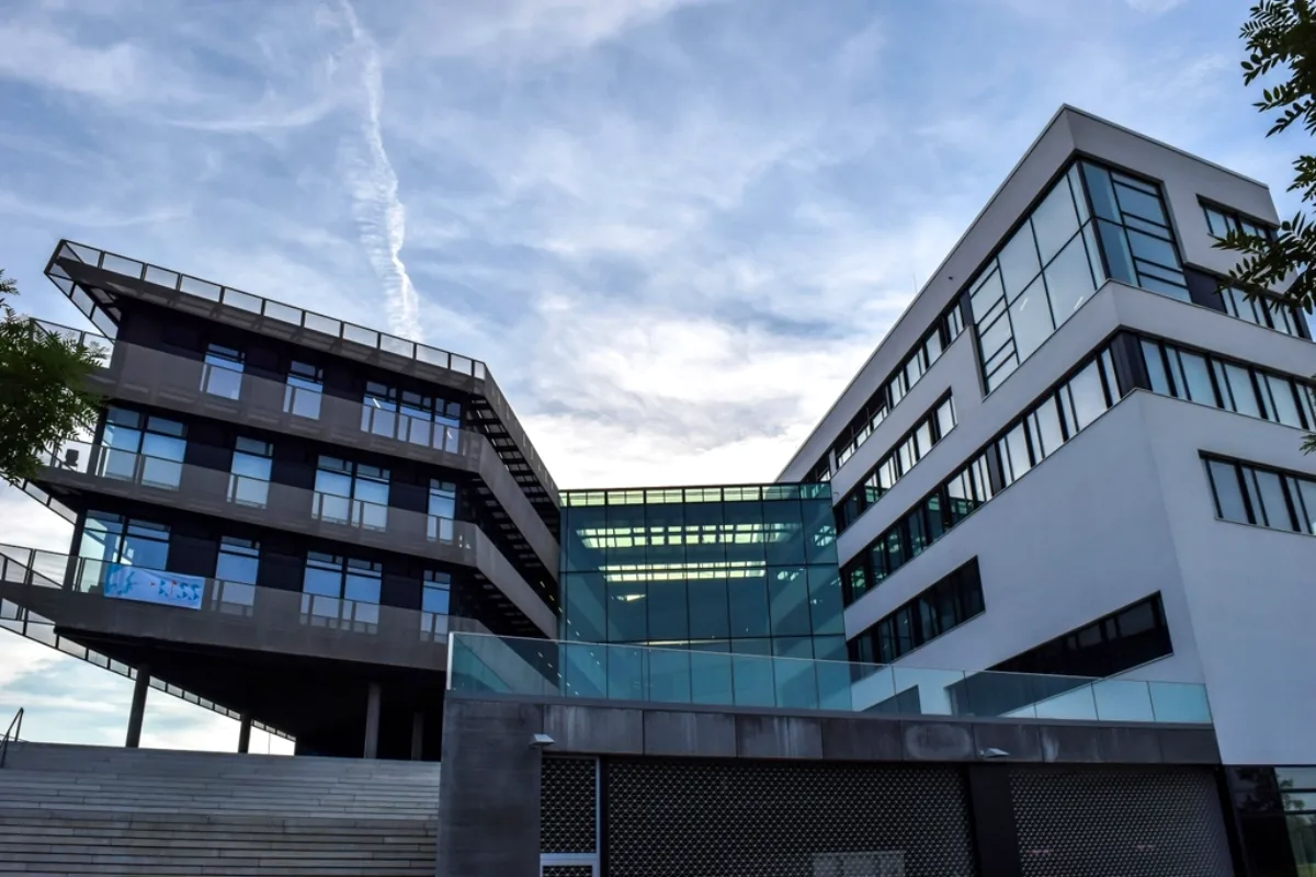 Modern university campus buildings with glass façades under a cloudy sky